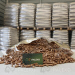 Pellet drzewny Gold worek rozsypany z wizytówką Paleko na tle palet w magazynie