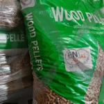 Worek pelletu cetim oparty o palety pelletu. Kolory: zielony, biały i brązowy.